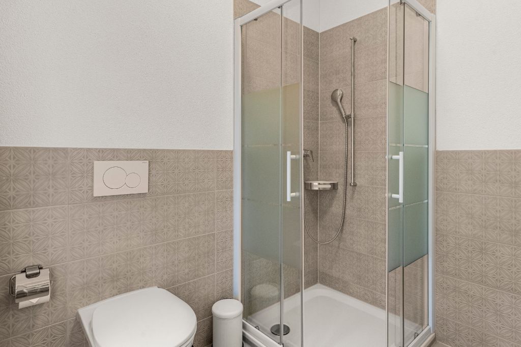 Een badkamer met een douchecabine van glas, een toilet en een handdoekdispenser.