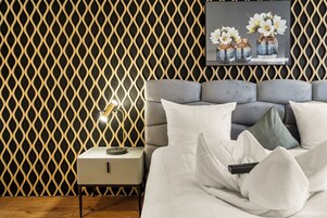 Un dormitorio moderno con pared estampada, cabecero tapizado gris, ropa de cama blanca y una lámpara de noche.