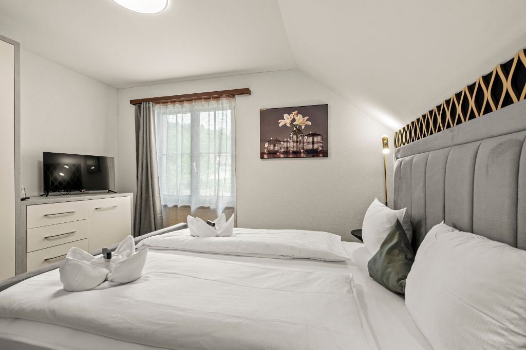 A hotel room with a bed, a TV, a desk, and a window with curtains.