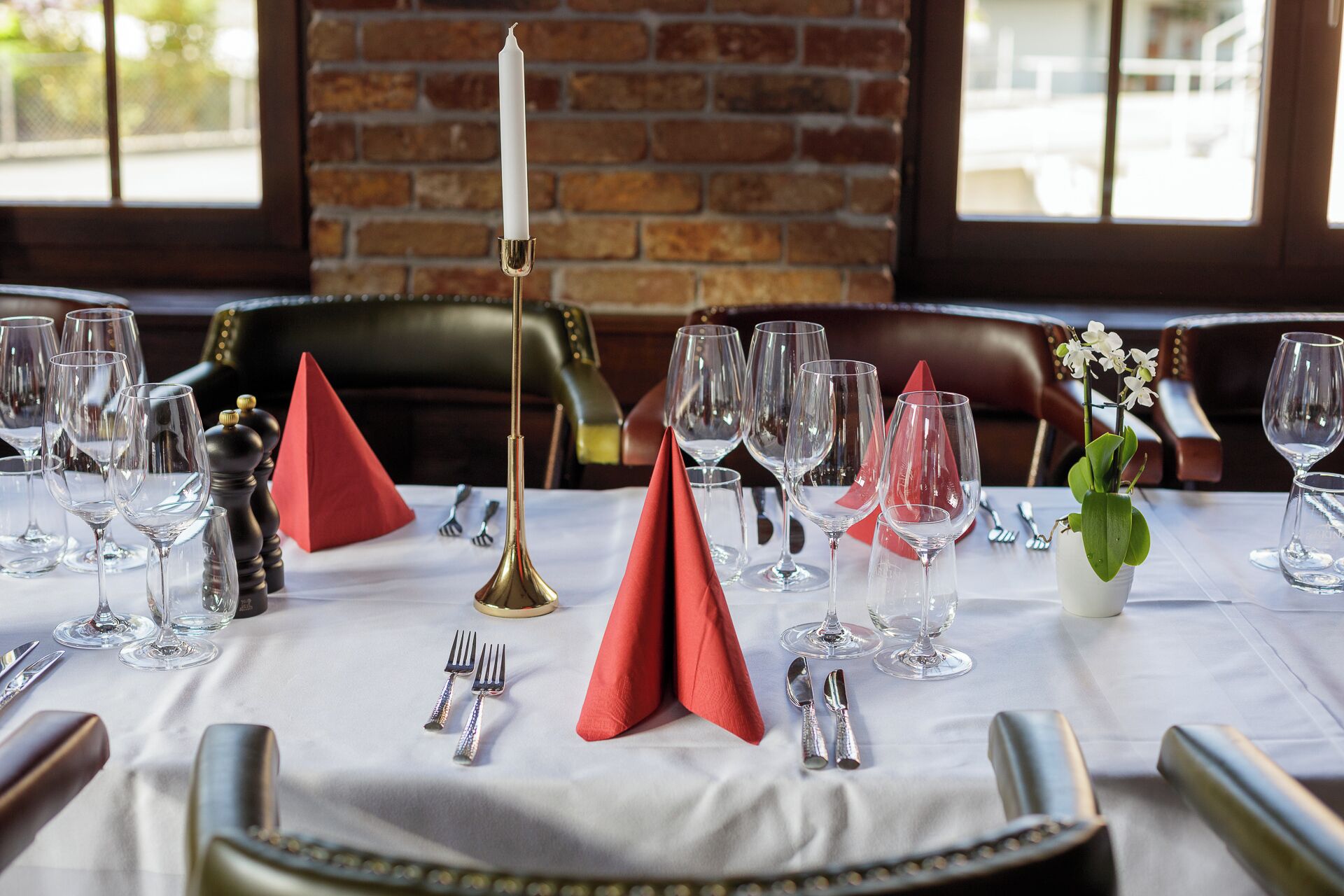 A restaurant table set with wine glasses, red napkins, and a candle.