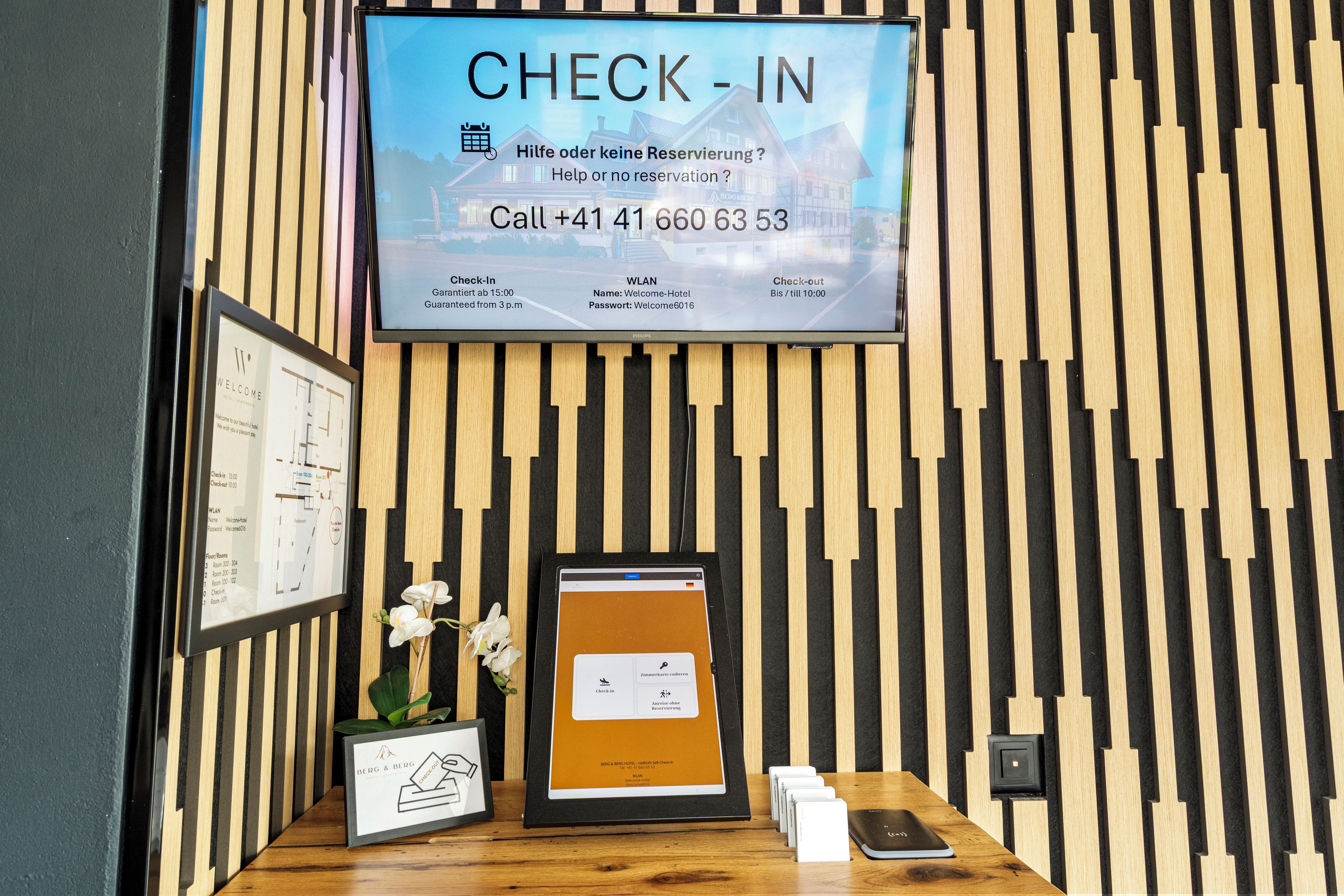 Un espace d’accueil d’hôtel doté d’un écran permettant d’effectuer l’enregistrement et affichant les disponibilités des chambres ainsi que les coordonnées.