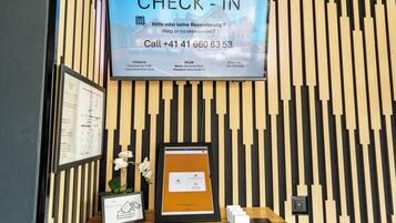 Zona de recepción de un hotel con una pantalla de registro mostrando disponibilidad de habitaciones e información de contacto.
