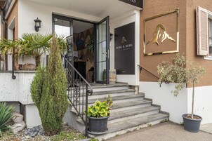 Entrada de un hotel con una escalera que lleva a la puerta, un cartel y plantas en macetas.