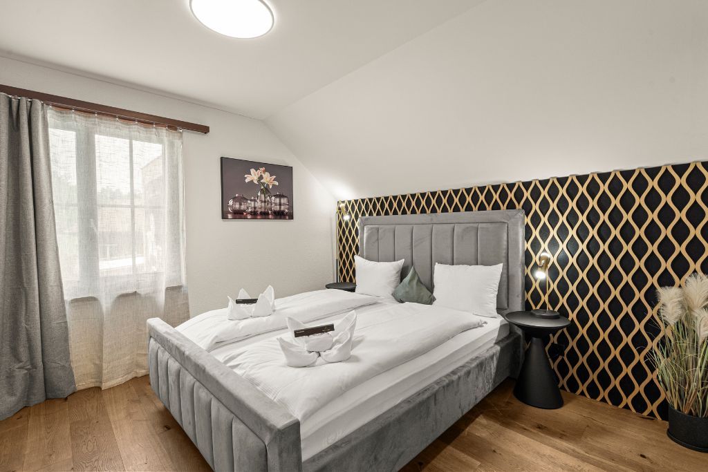Une chambre à coucher avec un grand lit, une table de chevet, une lampe et une fenêtre avec des rideaux.