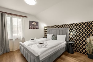 Un dormitorio con una cama grande, una mesita de noche, una lámpara y una ventana con cortinas.