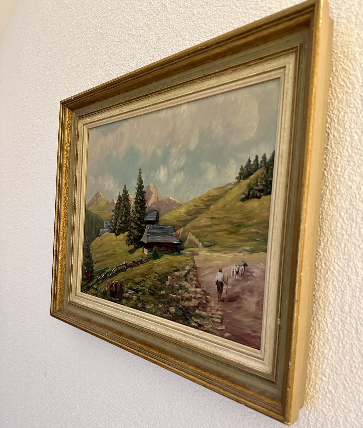 Ein gerahmtes Landschaftsbild mit einem Berg, einem Haus und einem Weg.
