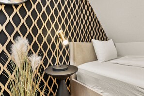 Un dormitorio moderno con pared de diseño geométrico, una mesita de noche con lámpara y una cama con ropa de cama blanca.