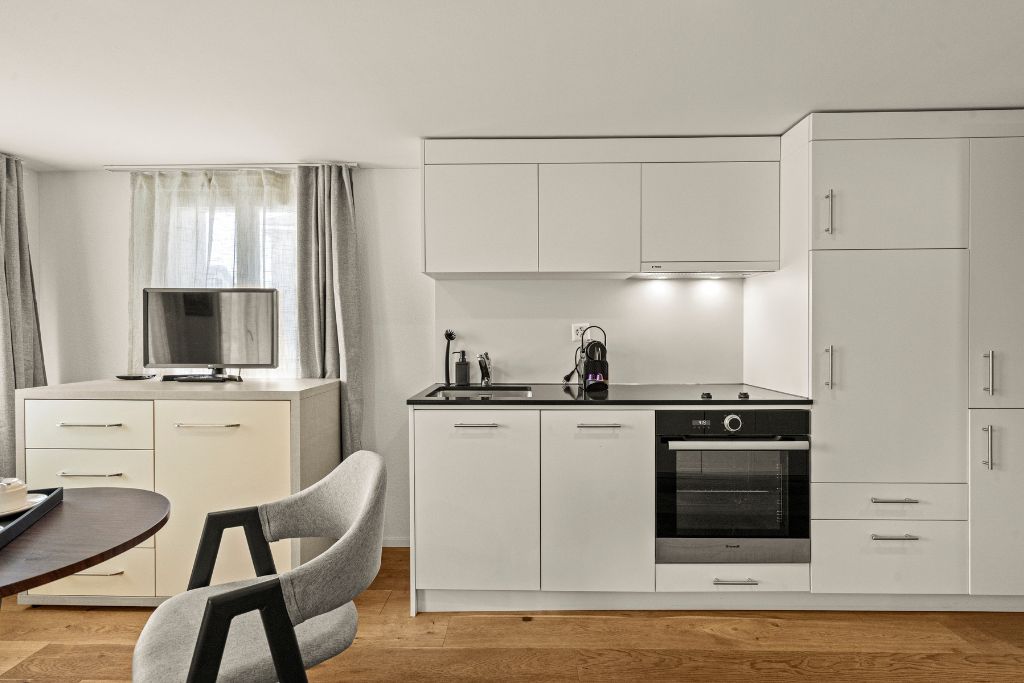 A modern kitchen with white cabinetry, a built-in oven, and a dining area with a table and chairs.