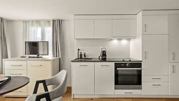 A modern kitchen with white cabinetry, a built-in oven, and a dining area with a table and chairs.