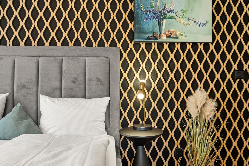 Une chambre à coucher avec une tête de lit rembourrée de couleur grise, une table de chevet ronde avec une lampe, et un tableau accroché au mur.