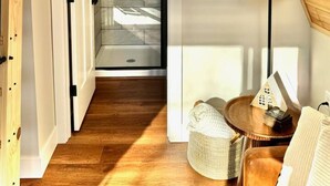 Interior de madera con una puerta de cristal que da a una zona con baldosas, una decoración con el símbolo de la paz tejido, y una pequeña mesa redonda con una lámpara.