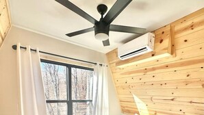 Un dormitorio con cama, ventilador de techo, ventana con cortinas y pared de madera.