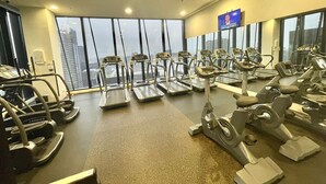 Une salle de sport équipée de tapis de course, de vélos elliptiques et d’un écran de télévision.