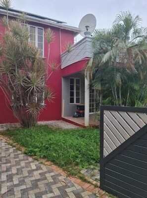 A red house with a satellite dish, a paved driveway, and a gated entrance. - Relax in peace and comfort in a 1-bedroom Flat in Christ Church with WiFi, AC (Oistins)