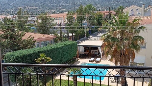 A balcony with a view of a residential area, including houses, a swimming pool, and a mountain in the background. - ATH AIRPORT LOFT PAIANIA (Peania)