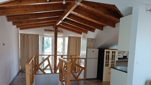 A spacious room with a high ceiling, wooden beams, a staircase, and a kitchen area with cabinets and a refrigerator. - ATH AIRPORT LOFT PAIANIA (Peania)
