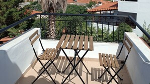 A balcony with a wooden table and chairs, a palm tree, and a view of a town with red-roofed buildings. - ATH AIRPORT LOFT PAIANIA (Peania)