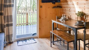 A wooden interior with a dining table set for two, a television mounted on the wall, and a view of a wooden fence and trees outside. - 1 bedroom accommodation in Hunmanby (Hunmanby)