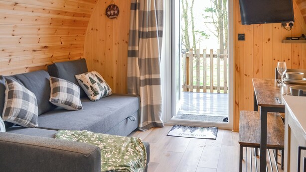 A cozy cabin interior with a sofa, a dining table, a TV mounted on the wall, and a view through a sliding door. - 1 bedroom accommodation in Hunmanby (Hunmanby)