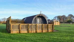 A small, round, wooden structure with a dark roof, surrounded by a wooden fence, set in a grassy field. - 1 bedroom accommodation in Hunmanby (Hunmanby)