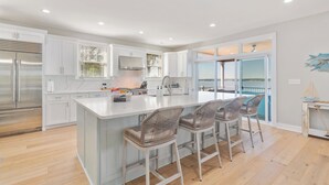 A modern kitchen with white cabinets, a stainless steel refrigerator, a large island with bar stools, and a view of the outdoors through a sliding glass door. - Gaston Shores / Boat Dock, Lake Access & Hot Tub (Littleton)