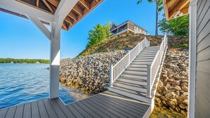 A wooden deck with a stone wall and a staircase leading to a house on a hill. - Gaston Shores / Boat Dock, Lake Access & Hot Tub (Littleton)