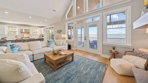 A spacious living area with a large window, a kitchen in the background, and a cozy seating arrangement. - Gaston Shores / Boat Dock, Lake Access & Hot Tub (Littleton)