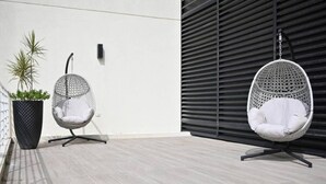 Een modern buitenverblijf met twee witte, eivormige stoelen en een grote plantenbak met een beplanting.