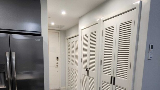 Een moderne keuken met een roestvrijstalen koelkast, een wit aanrecht met een kom, een wijnglas en een mes. Er zijn witte, horizontale kasten langs de muur.
