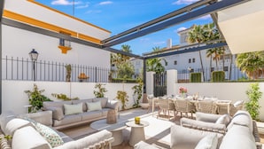 Une terrasse extérieure ensoleillée, aménagée avec un canapé, des fauteuils et une table à manger.