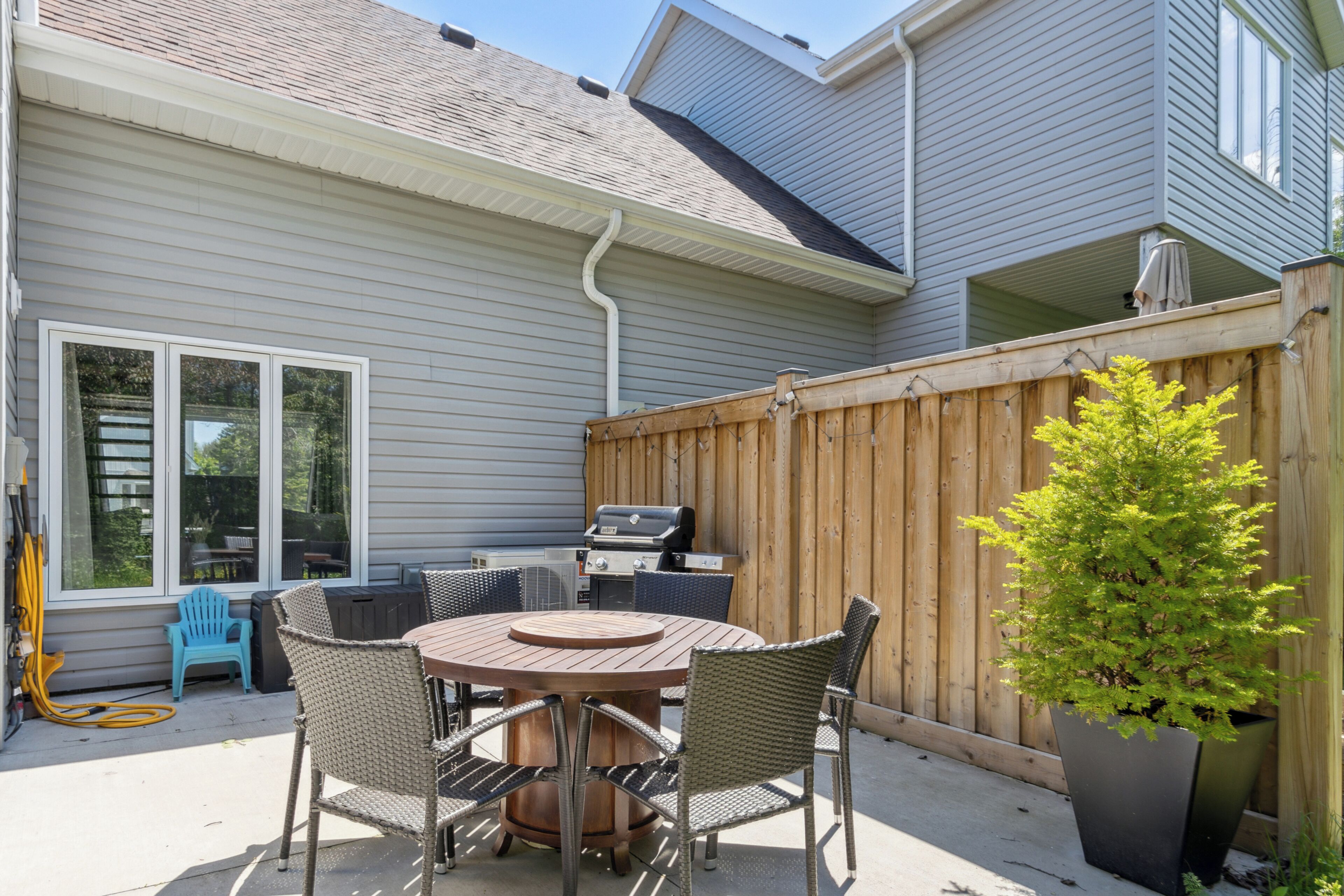 A patio with a round table and chairs, a grill, and a wooden fence.