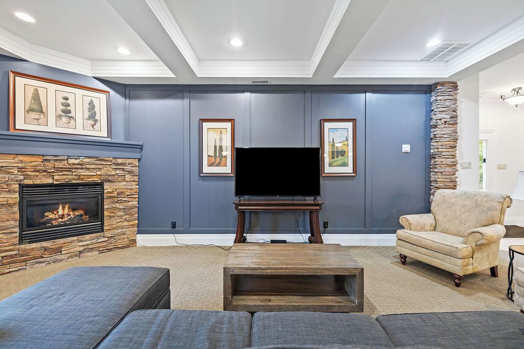Una sala de estar con chimenea de piedra, un televisor de pantalla plana, un sillón beige y un amplio sofá modular.