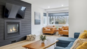 En moderne stue med pejs, to sofaer, et sofabord og et tv ophængt på væggen.