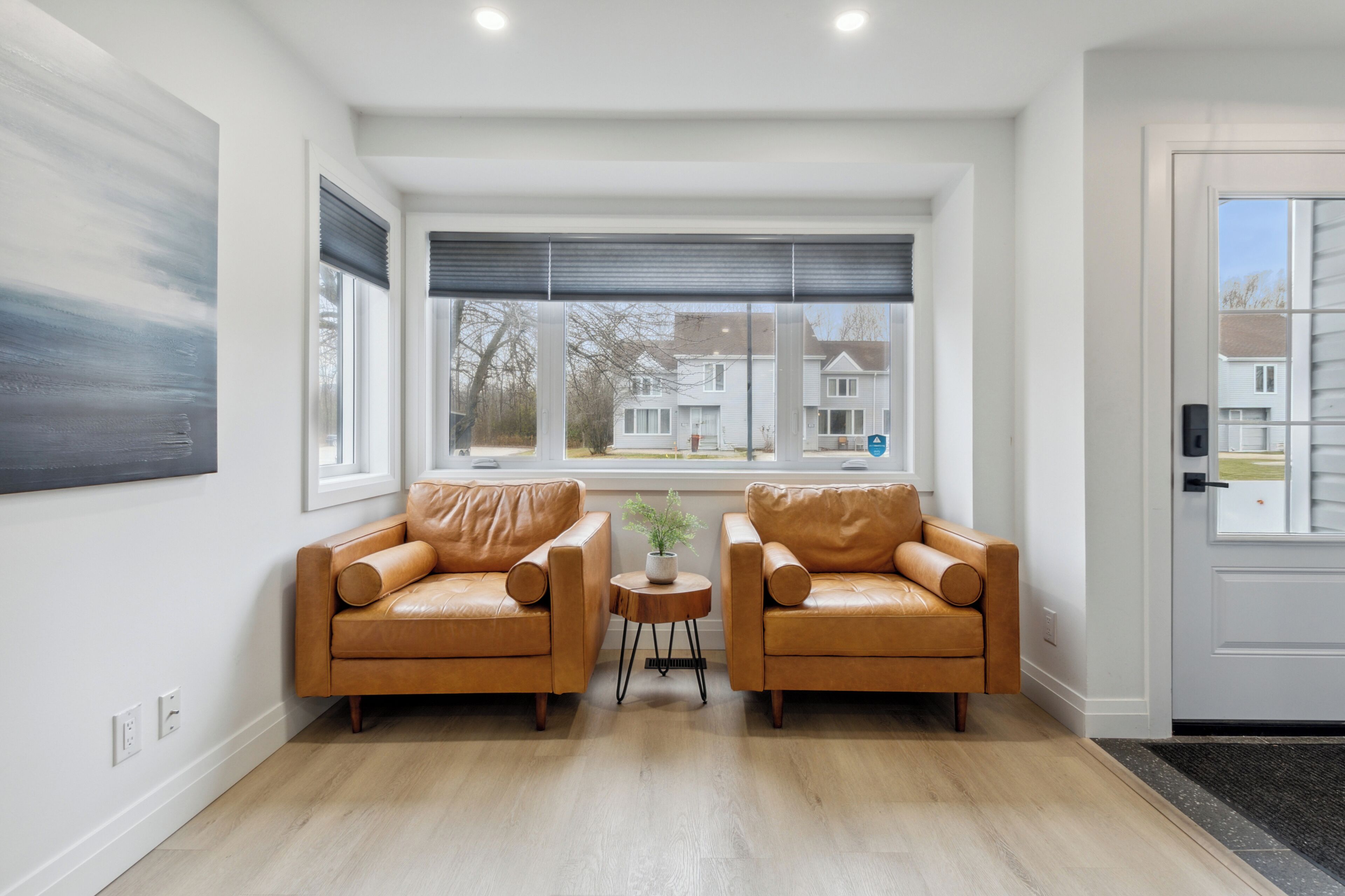 A modern living room with two leather sofas, a small round table with a plant, and large windows with blinds.