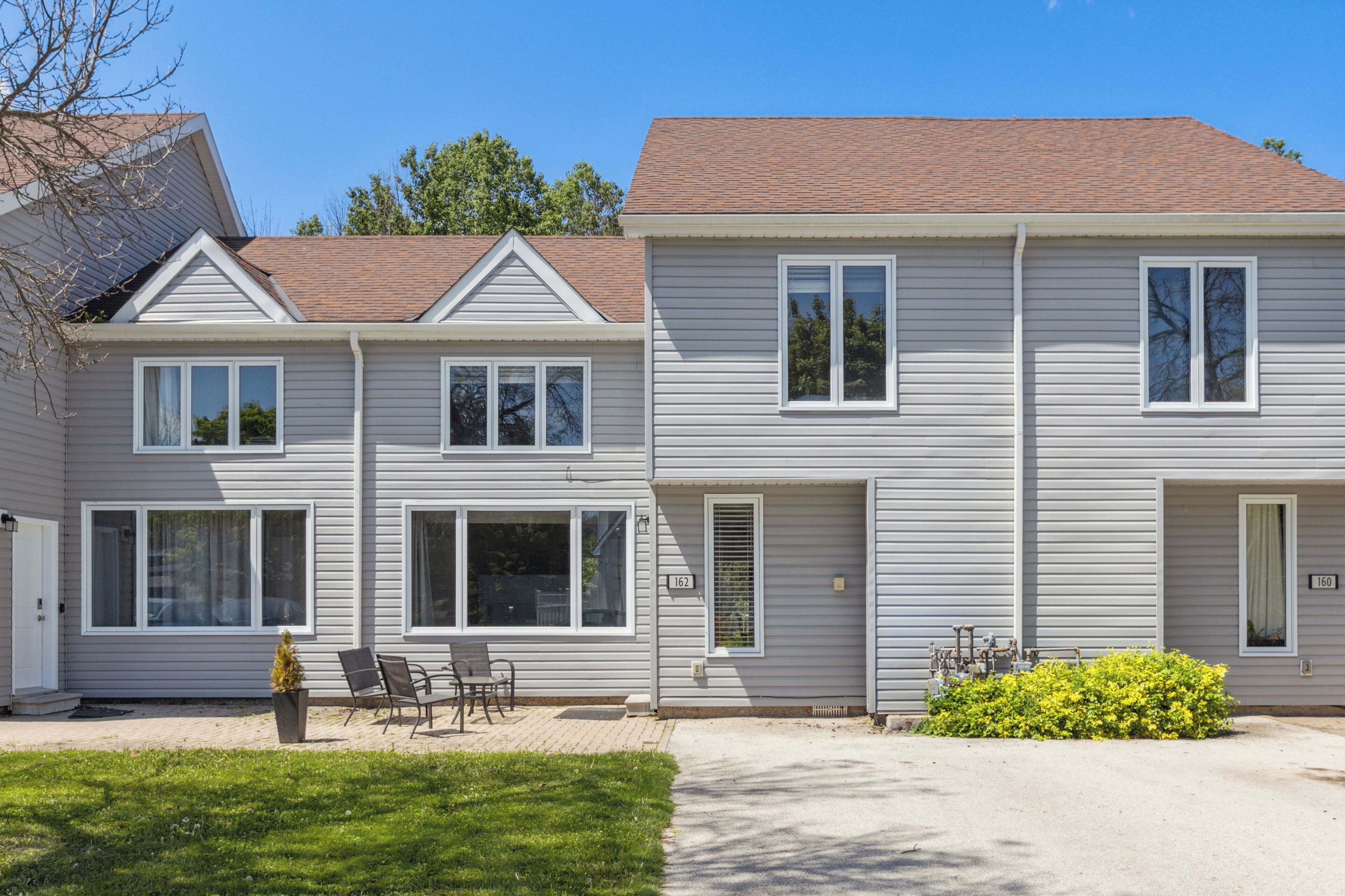 A two-story residential building with a front porch, large windows, and a well-maintained lawn.