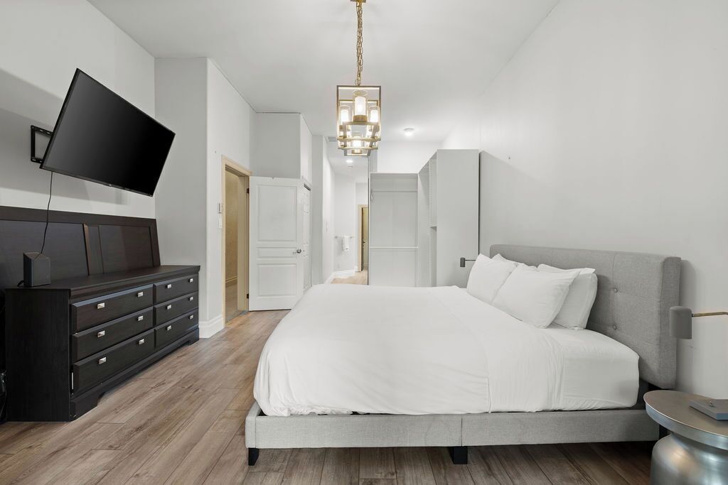 Un dormitorio moderno con una cama grande, un aparador oscuro, un televisor de pantalla plana en la pared y una araña.