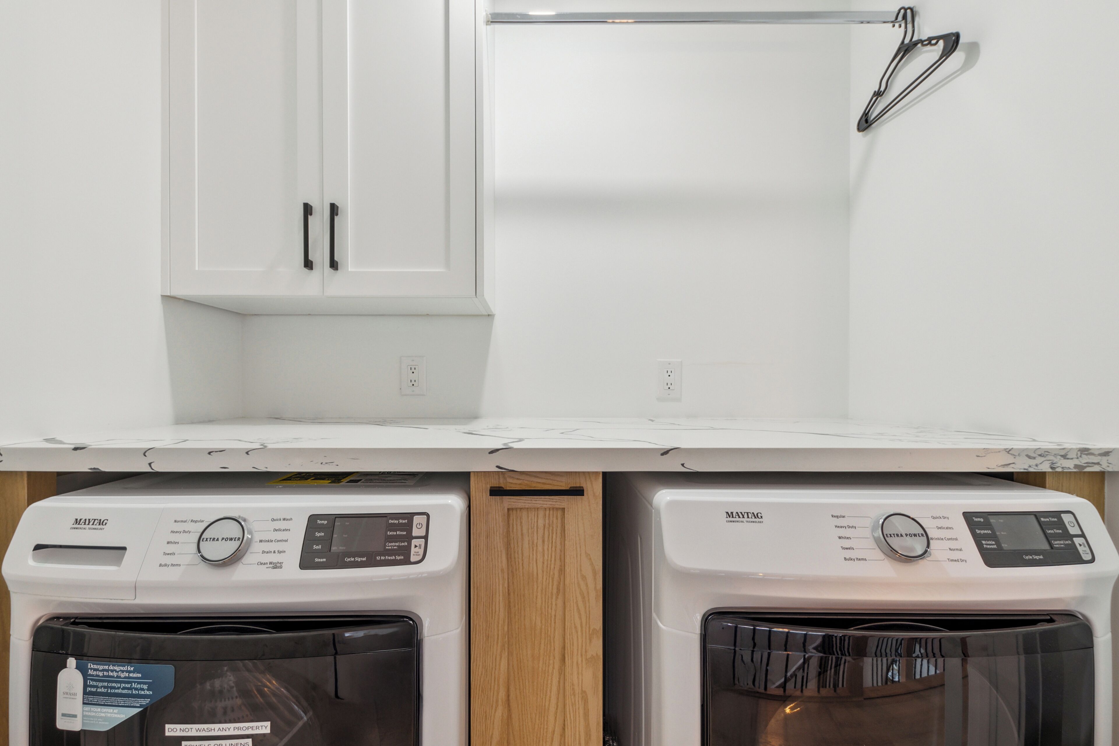 A laundry area with two Maytag washing machines, a wooden cabinet, and a white countertop.