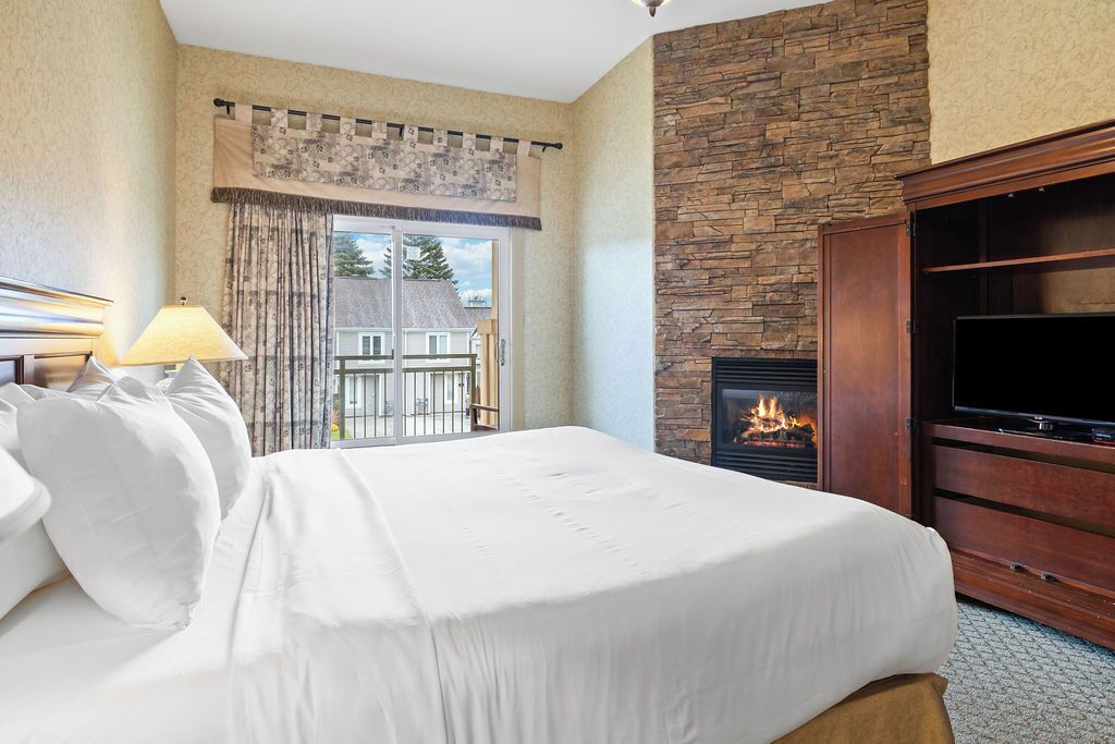 Une chambre d’hôtel avec un lit, une télévision, une cheminée et un balcon avec des rideaux.