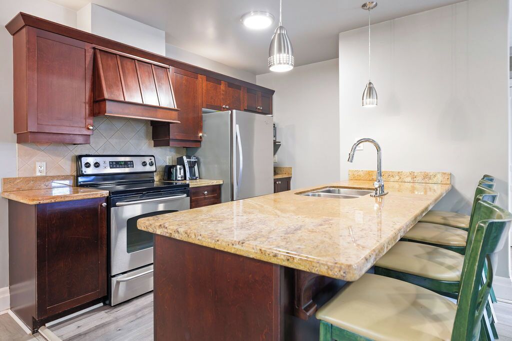 A kitchen with dark wooden cabinets, a stainless steel refrigerator, a built-in oven, a granite countertop, and a sink with a modern faucet.