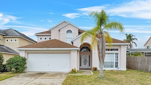 A single-story house with a garage, a front entrance with an arched doorway, and a small front yard with a palm tree and a wooden fence.