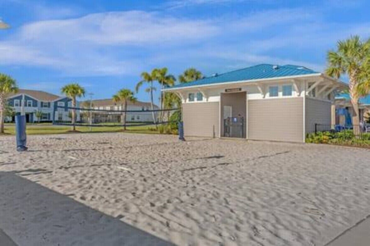 A beachside building with a covered entrance, a sandy area in front, and palm trees in the background.