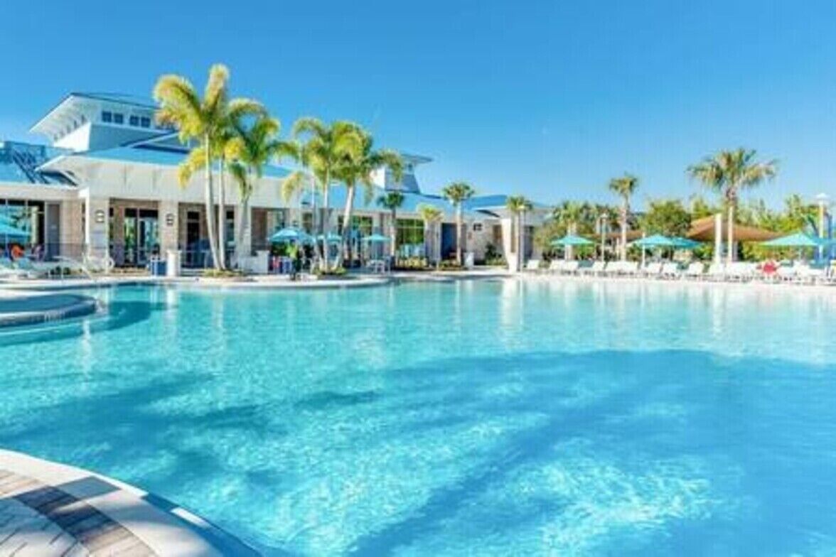 A hotel pool area with clear blue water, palm trees, and umbrellas.
