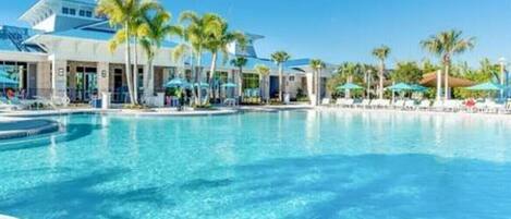 A hotel pool area with clear blue water, palm trees, and umbrellas.