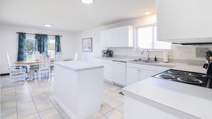 Una cocina moderna con armarios blancos, una isla central y un área de comedor con sillas blancas.