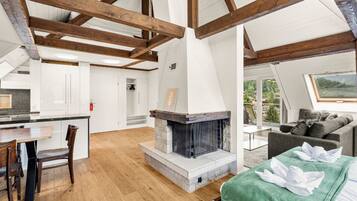 A modern loft with exposed wooden beams, a fireplace, a dining area, and a view of the outdoors.
