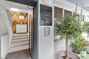 A hotel entrance with a staircase leading to a reception area, a wall-mounted directory, and a potted tree.