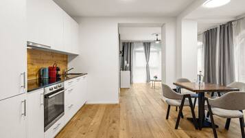 Une cuisine moderne avec des meubles blancs, un plan de travail en bois et un coin repas comprenant une table et des chaises.