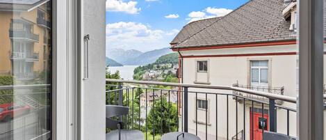 Ein Balkon mit Blick auf einen See und Berge, mit einer roten Tür, einem kleinen Tisch und einem Stuhl.