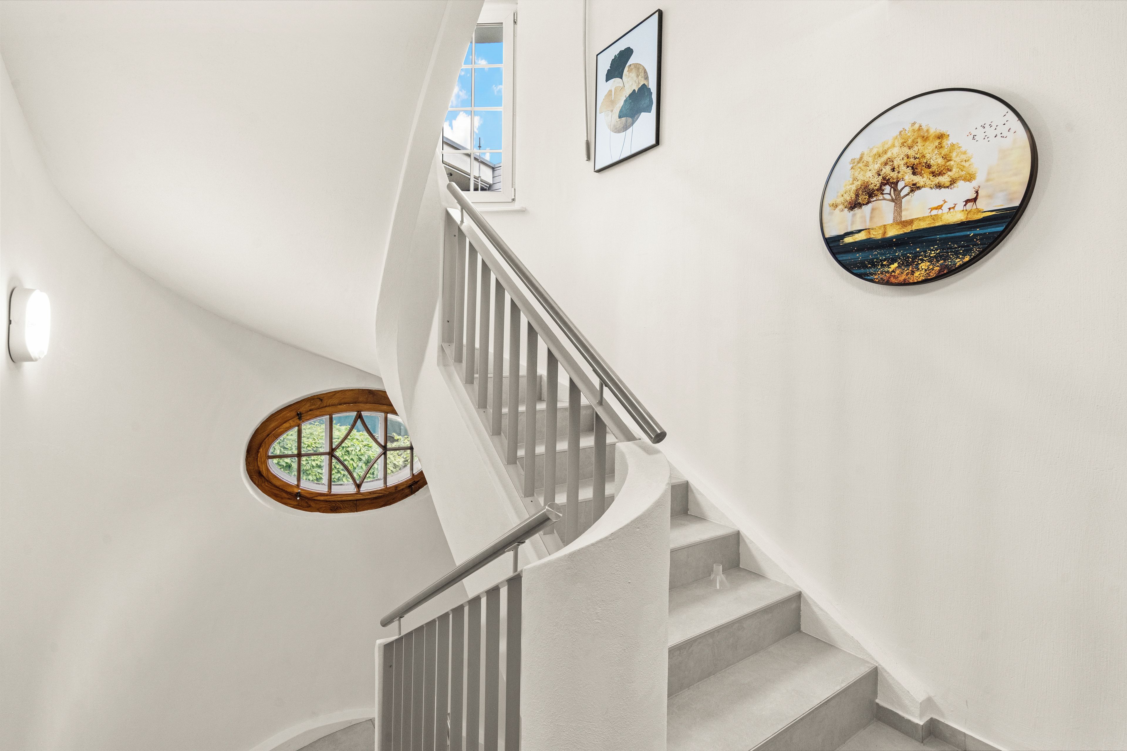 A staircase with a handrail, a window with a wooden frame, and two framed artworks on the wall.