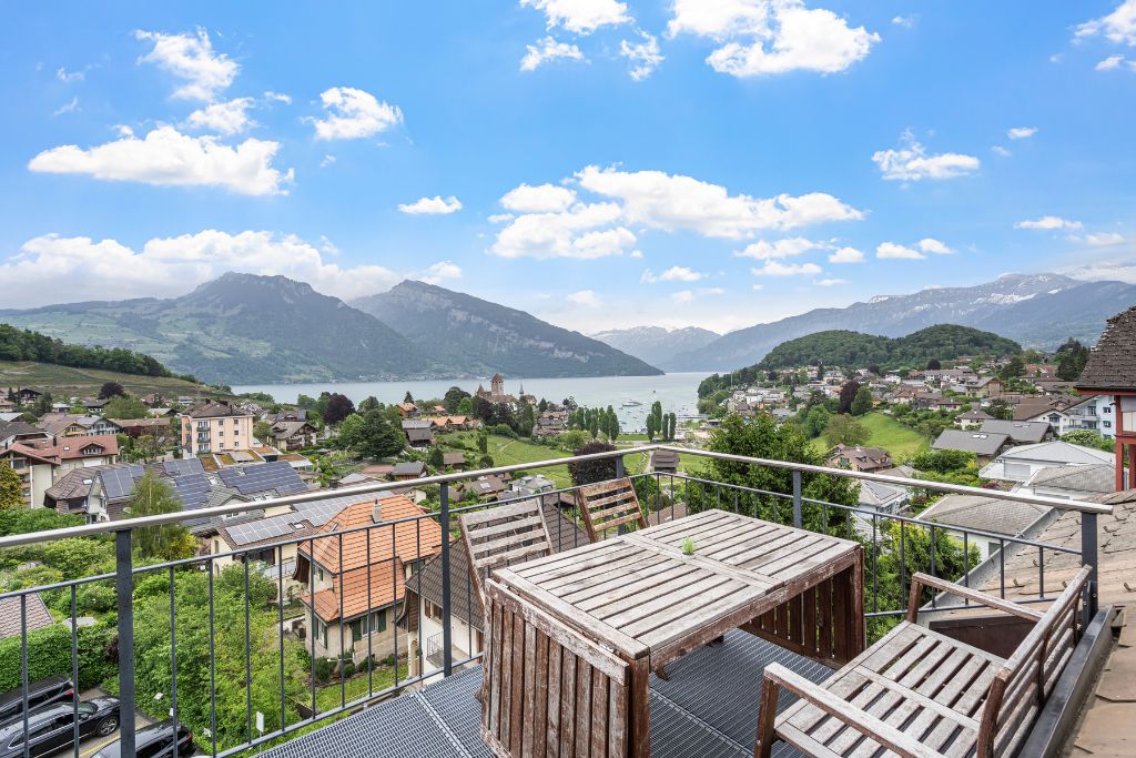 A balcony with a view of a lake, mountains, and a village.
